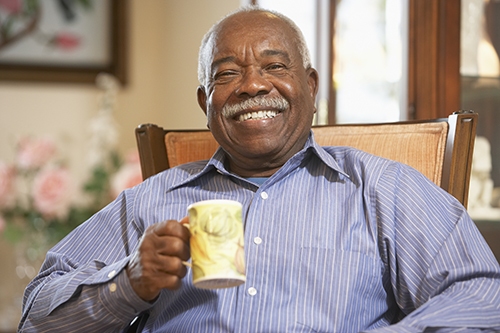 African american elderly man sitting in a chair and holding a cup of coffee